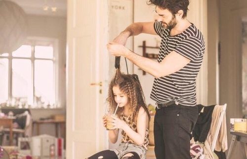 Father coparenting his daughter by tending to her hair.