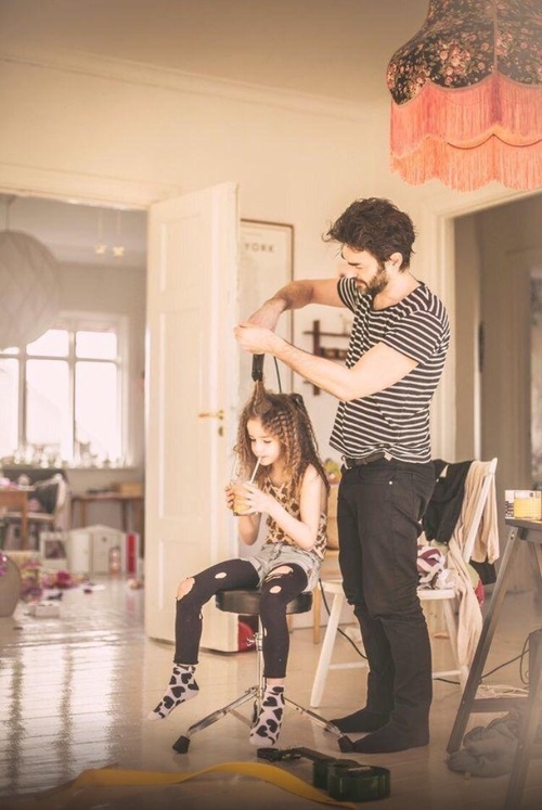 Father coparenting his daughter by tending to her hair.