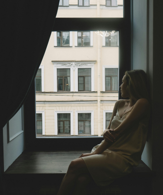 A woman sitting alone by a window, looking out thoughtfully, reflecting on the question of how can I afford to live alone after divorce.