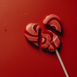 Broken heart-shaped lollipop on a red background, symbolizing the dissolution of a marriage