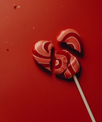 Broken heart-shaped lollipop on a red background, symbolizing the dissolution of a marriage