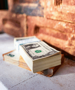Stack of U.S. dollar bills placed on a ledge beside a brick wall, symbolizing hidden or undisclosed financial assets in the context of divorce.