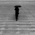 A woman walking alone up wide stone steps under an umbrella, symbolizing the emotional weight and uncertainty of contemplating divorce.