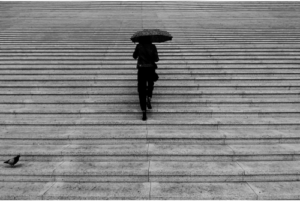 A woman walking alone up wide stone steps under an umbrella, symbolizing the emotional weight and uncertainty of contemplating divorce.