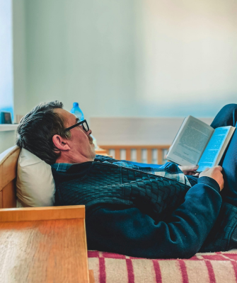 Man lying on a bed reading a book, representing comfort and staying in a familiar but unhappy marriage