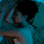 A woman lying alone in bed at night, resting on her side under soft blue lighting, capturing the quiet emotion of feeling alone after divorce.