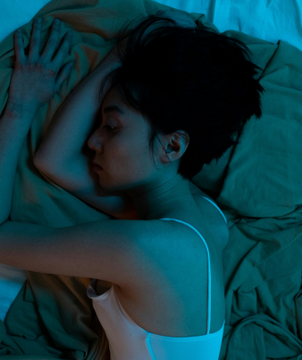A woman lying alone in bed at night, resting on her side under soft blue lighting, capturing the quiet emotion of feeling alone after divorce.