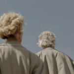 Back of a gray-haired man and woman in raincoats.