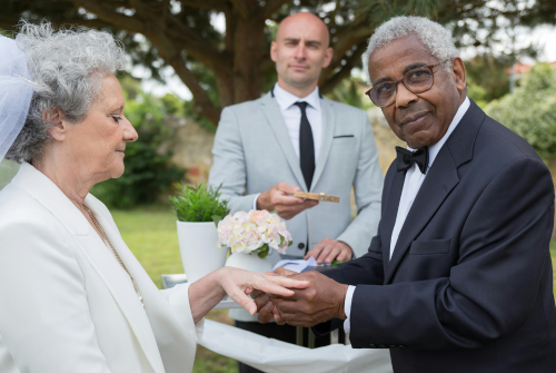 Older couple exchanging rings during an outdoor wedding ceremony, representing common law marriage and long term commitment.